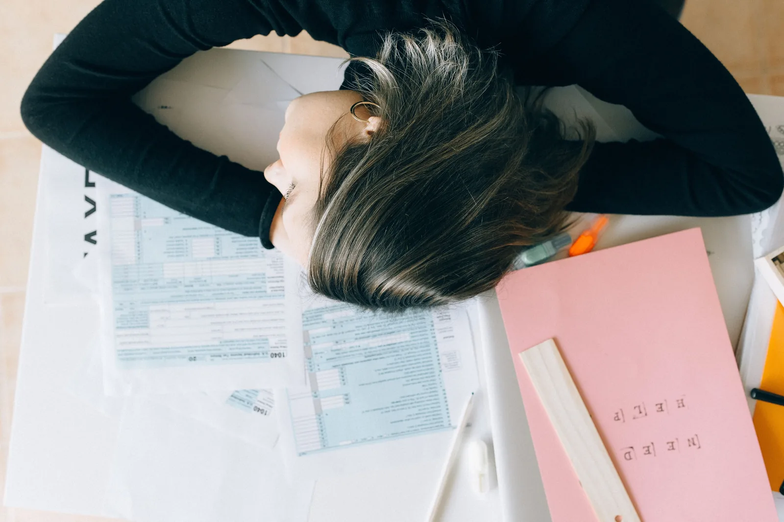 Woman resting her head on a desk covered in paperwork, showing the overwhelm of ADHD and perimenopause symptoms colliding