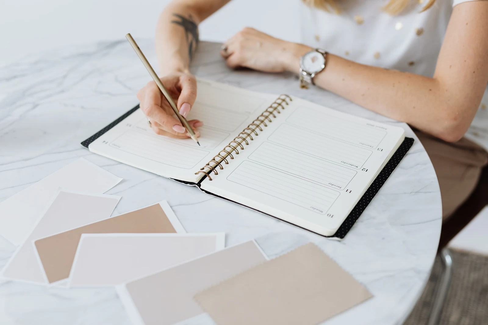 Woman writing in a planner at a table, doing the between-session work that coaching depends on