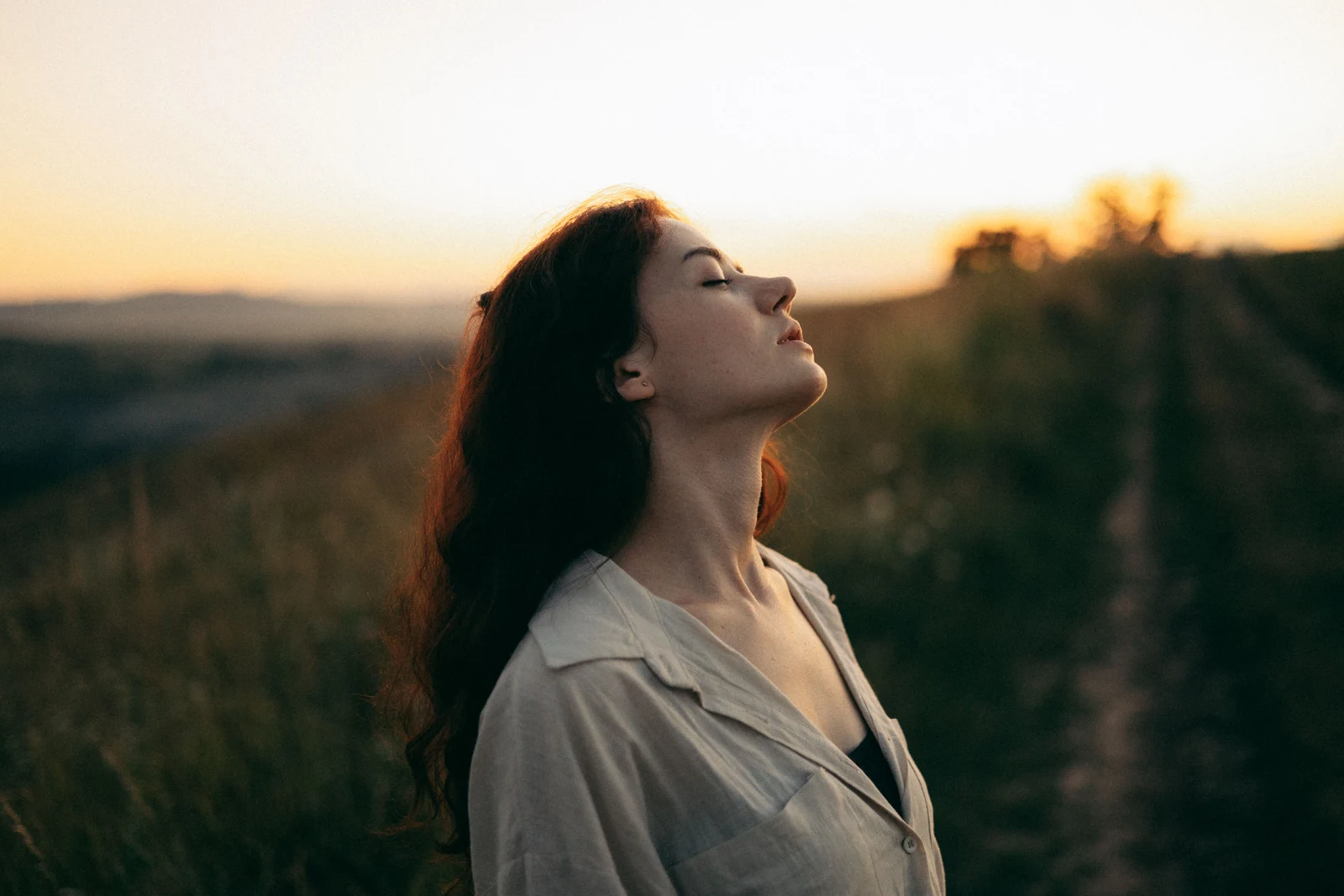 Woman standing outdoors with her eyes closed at sunset, taking a pause before reacting
