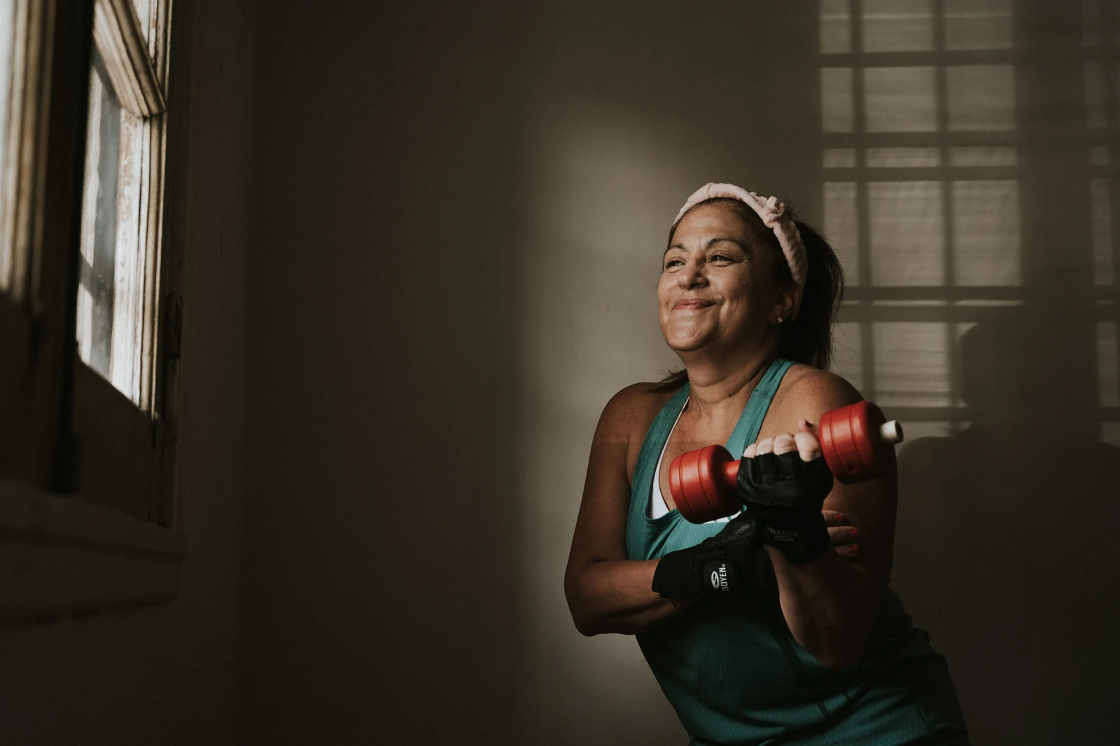 Smiling middle-aged woman lifting light dumbbells at home, showing strength training during perimenopause